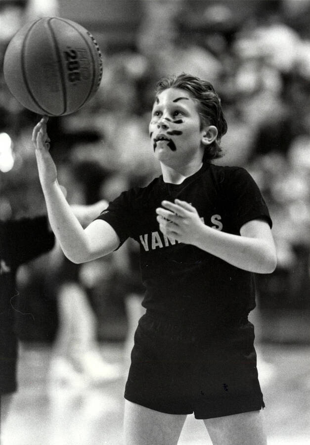 A student wearing face paint spinning a basketball on their finger.