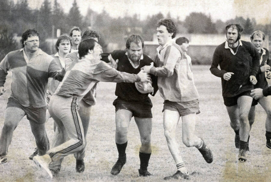 Men playing rugby. The man with the ball is Bob Campbell.