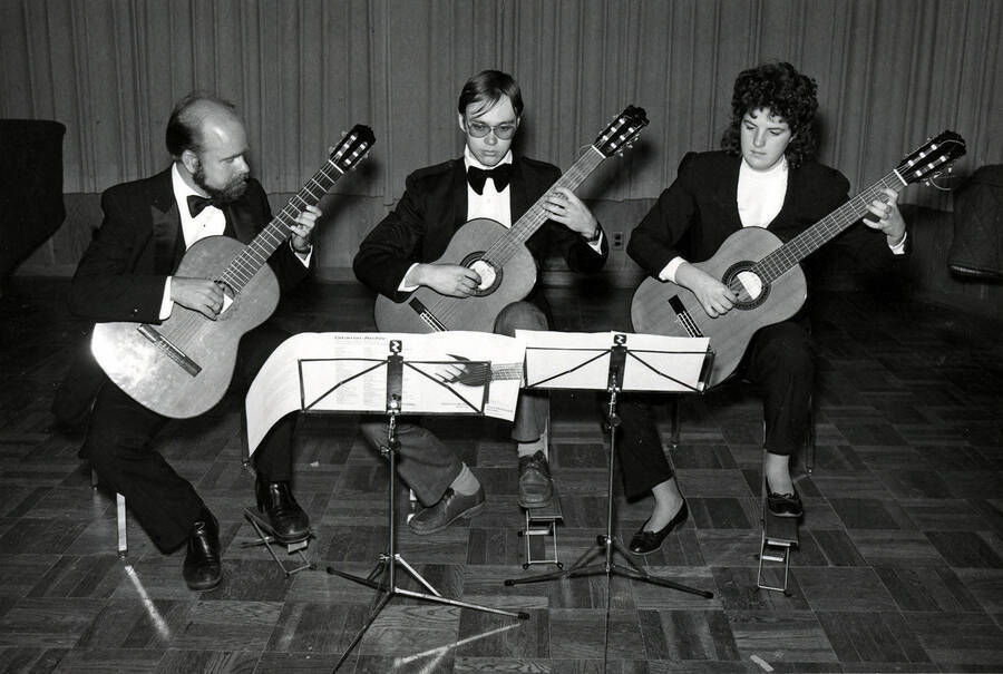 Three musicians performing on classical guitars.