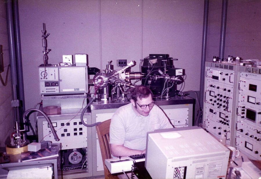 A man working on an early computer and surrounded by various scientific equipment.