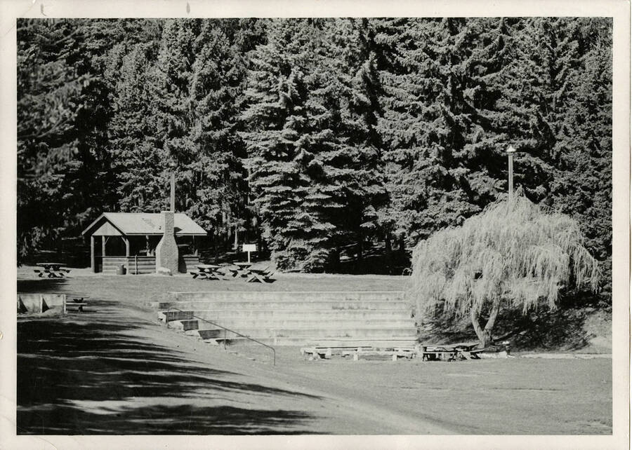 Outdoor recreational area in the Shattuck Arboretum on the University of Idaho campus. Facility includes picnic tables, a building, and a sitting area surrounded by trees.