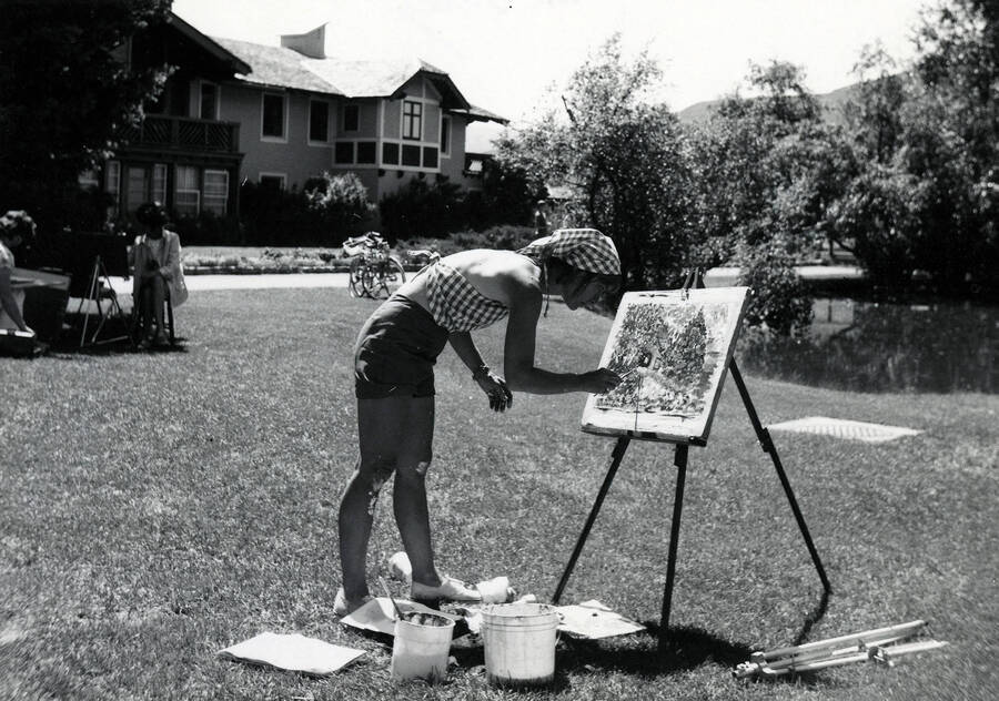 Mary Blanton painting outdoors. Captions on the back read: ""UI Workshop on Wheels. Black and White #1 by Helen Cross, early 1970s""; ""Sun Valley""; ""Mary Blanton, Moscow - wife of Paul Blanton, head of UI Art & Architecture Dept.""