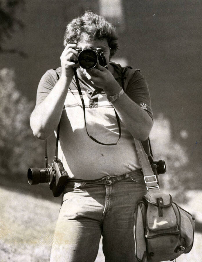 Bob Bain, Communications department, holding a camera and taking a photograph.