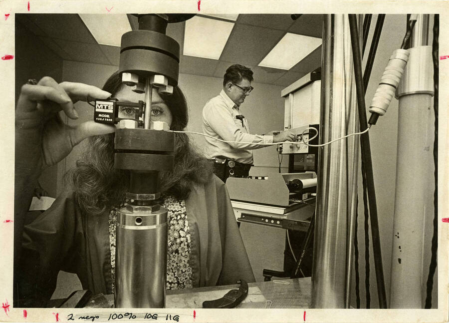 A man and woman operating engineering equipment. Note on back of photo says: ""Don't use - no protective goggles.""