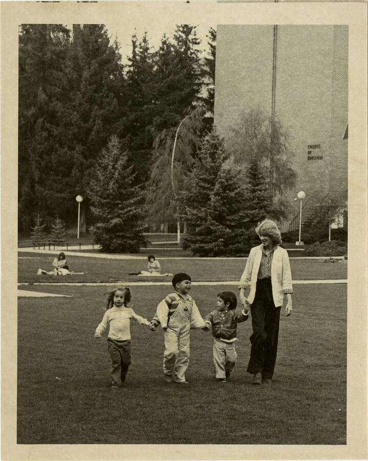 Three children and one woman walking on the lawn in front of the College of Education Building on the University of Idaho Campus.