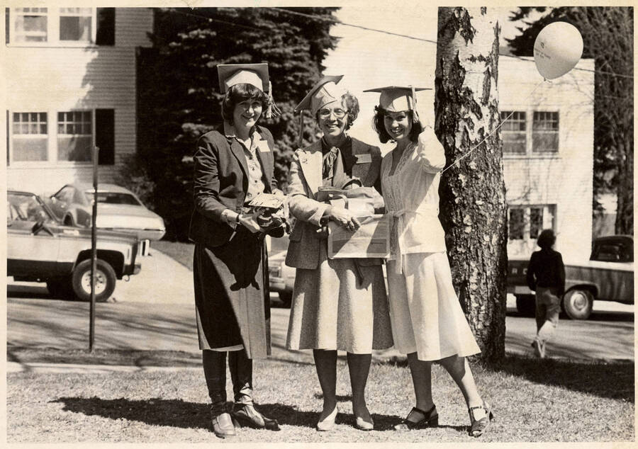 Three alumnae wearing mortar boards and holding a turtle and balloon.
