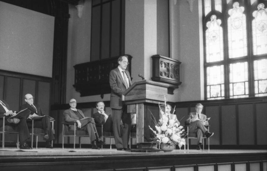 A man speaking at a podium with President Gibb seated behind (left).