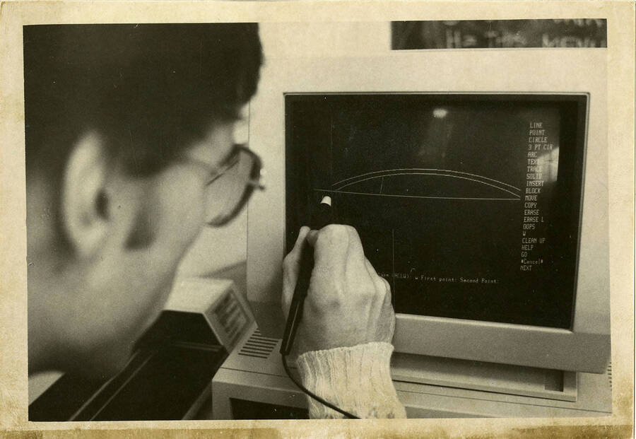 A man drafts on an architecture computer. Computer screen reads: ""Line - Point - Circle - 3 Pt Circle - Arc - Text - Trace - Solid - Insert - Block - Move - Copy - Erase - Erase L - Oops - W - Clean Up - Help - Go - Cancel - Next.""