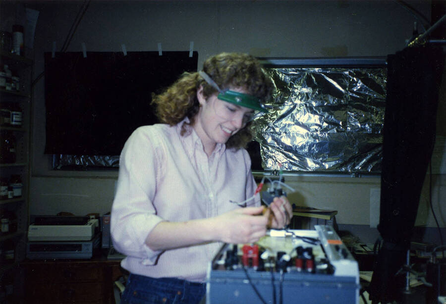 A woman working with scientific equipment and wearing protective glasses.