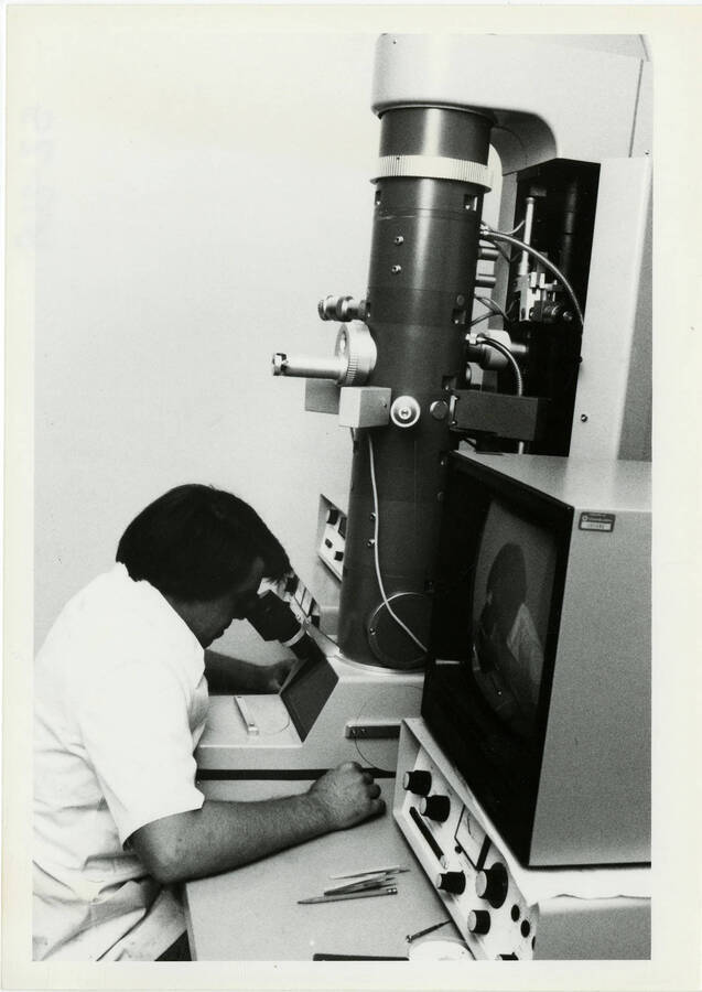 A man looking through a gigantic binocular microscope.