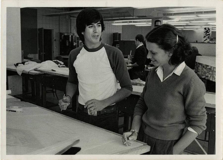 Two students, one male and one female, sketching a building in a classroom.