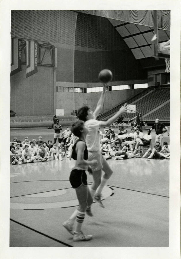 Two basketball players playing on the court. One is shooting the ball into the hoop.