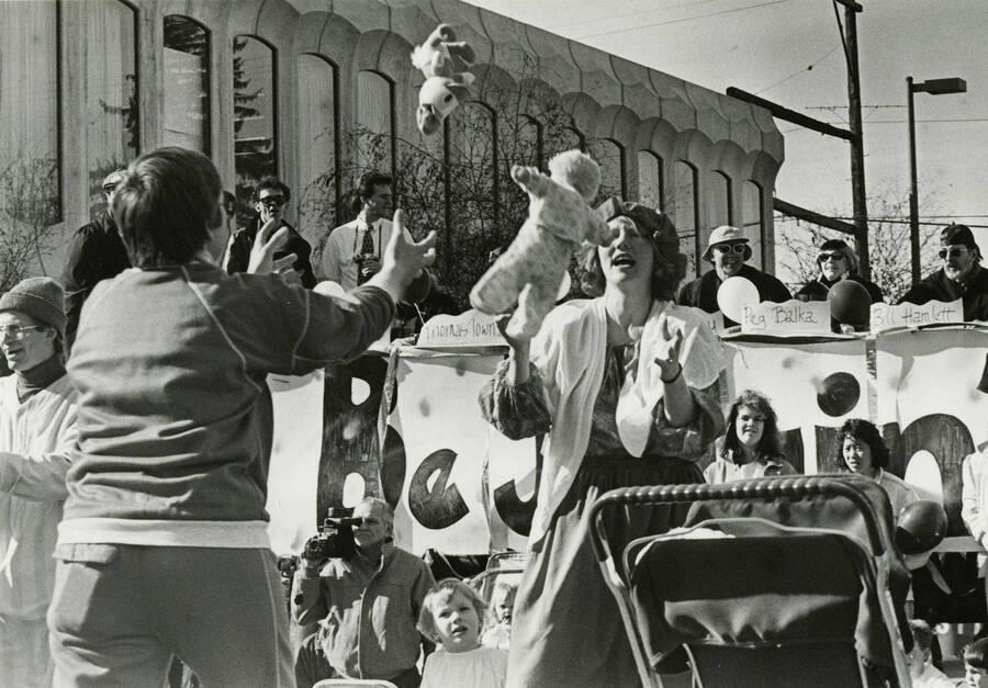 Two women tossing a baby doll and Donald Duck toy back and forth during a parade on Main Street, on the south side of the 3rd Street and Main Street intersection.