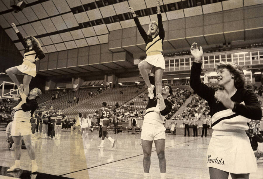 Four cheerleaders stoking the crowd at a basketball game in the Kibbie Dome. Written on the front of the photo is ""Cheerleader Illus.""