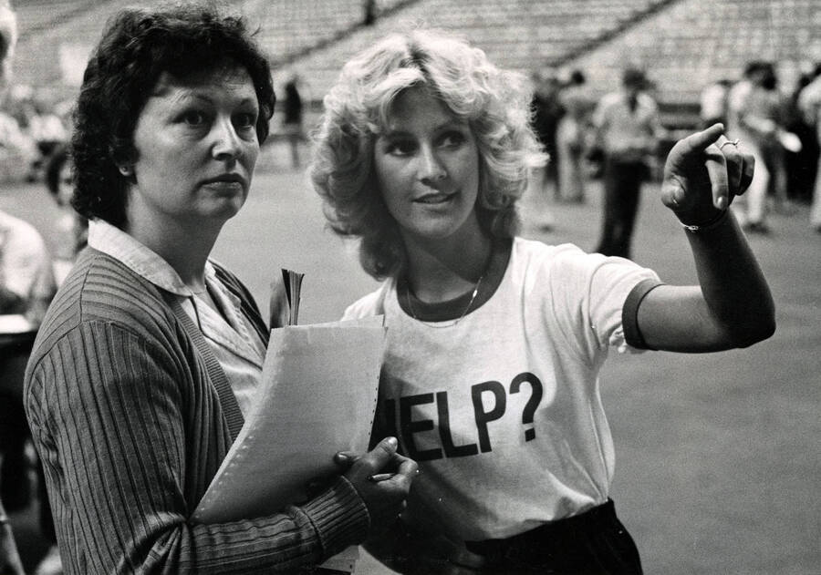 A woman wearing a shirt that says ""Help?"" assisting another woman during Registration Day 1985 in the Kibbie Dome.