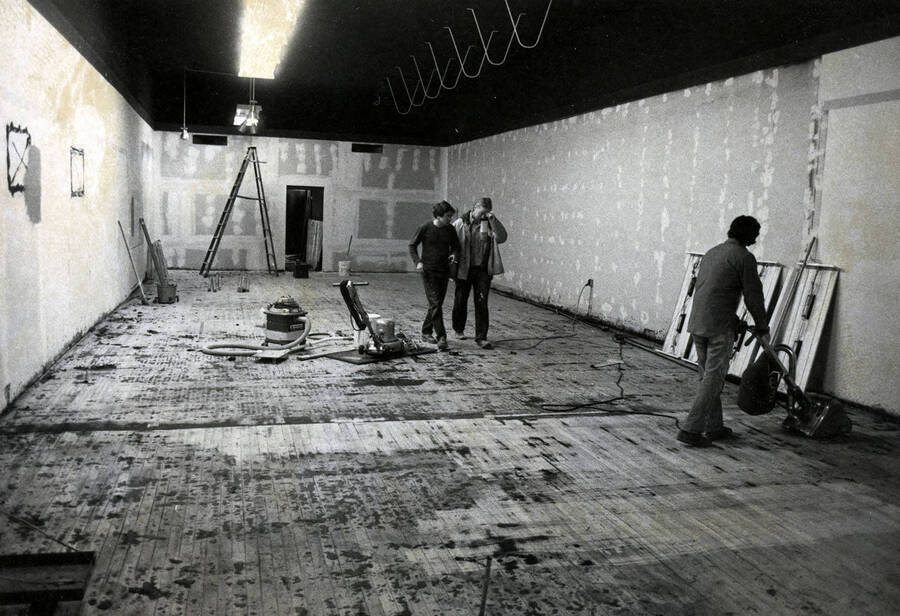 Interior of building under renovation with three individuals at work (possibly the Prichard Art Gallery).