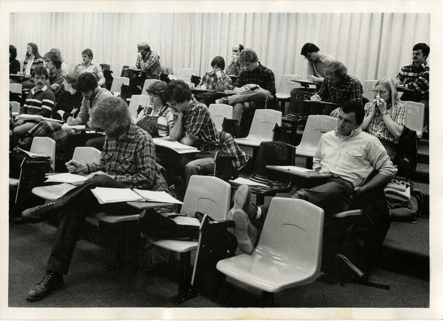 Students taking notes at desks in a classroom. Photo for publication, possibly a brochure, in which text ""There's a place just for you"" was placed in empty chair.