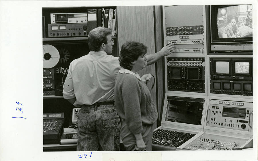A man and woman operating audio and visual equipment. A baby is on the screen in the  right upper corner.