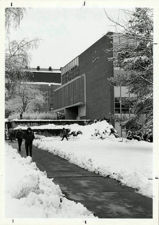 Winter scene of the University of Idaho Library before the 1993 remodel. Students walk on sidewalks cleared of snow.
