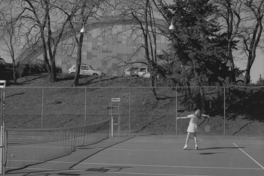A student playing tennis on the courts just outside of the Physical Education Building.