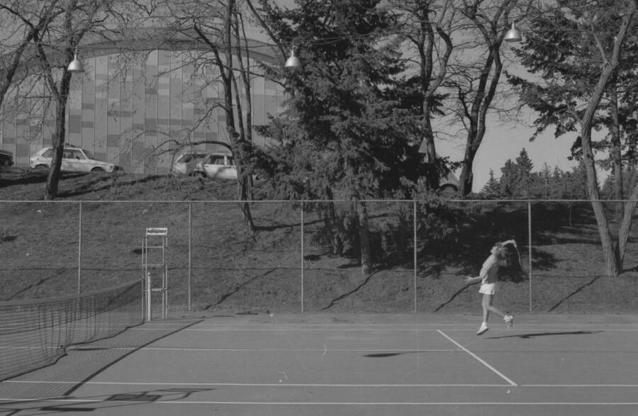 A student playing tennis on the courts just outside of the Physical Education Building.
