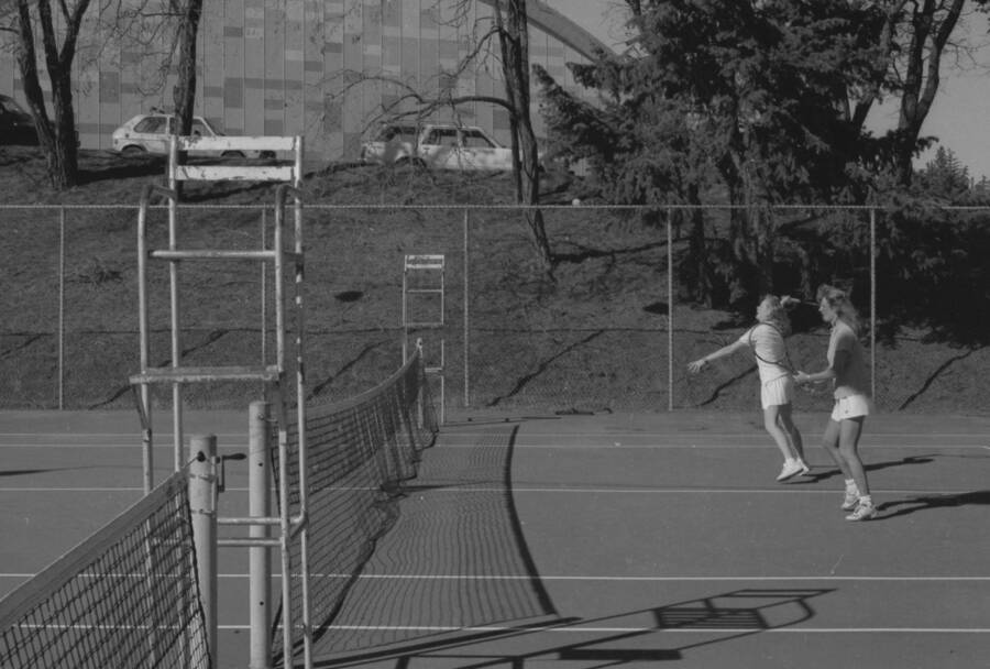 Two students playing tennis on the courts just outside of the Physical Education Building.