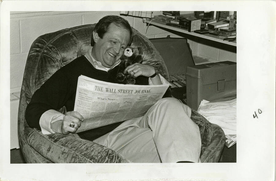 Bruce Pitman, holding a teddy bear to his face and reading the Wall Street Journal, at Shoup Hall during an overnight S.A.S. visit.