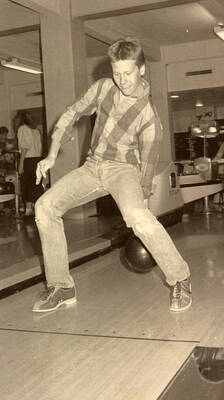 Student bowling, rolling the ball between his legs.