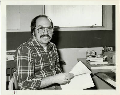 Joseph Marcello sitting and posing with papers in his hand.