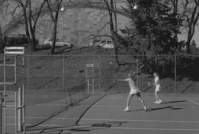 Two students playing tennis on the courts just outside of the Physical Education Building.