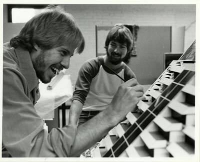 Two male students building an architectural model in a classroom.