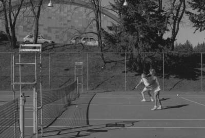 Two students playing tennis on the courts just outside of the Physical Education Building.