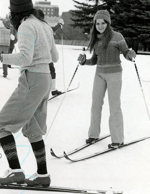Two students skiing on campus, with the Theophilus Tower in the far background.