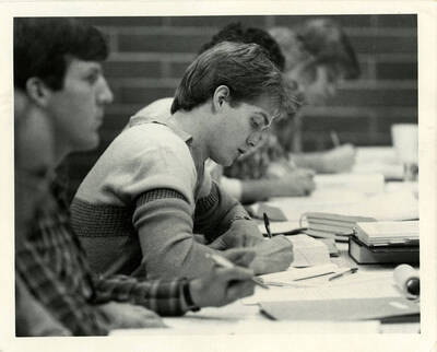 Students taking notes at a long desk or table.