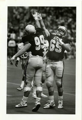 Idaho football players, wearing jerseys numbers 65 and 99, cheering.