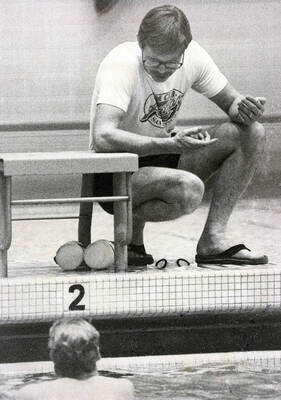 Coach at edge of pool speaking to swimmer in water.