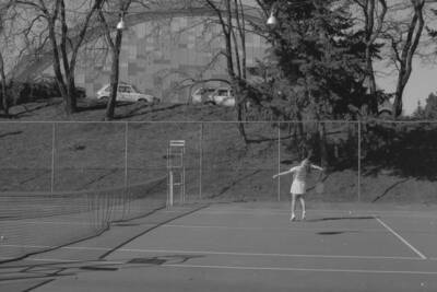 A student playing tennis on the courts just outside of the Physical Education Building.