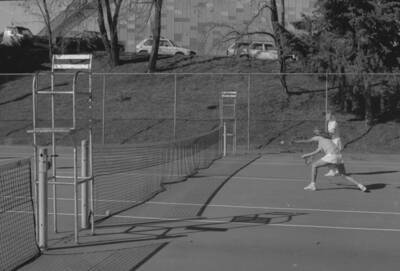 Two students playing tennis on the courts just outside of the Physical Education Building.