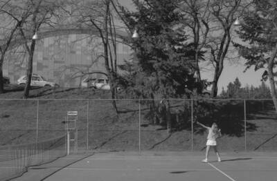 A student playing tennis on the courts just outside of the Physical Education Building.