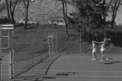 Two students playing tennis on the courts just outside of the Physical Education Building.
