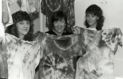 Three people displaying tie-dyed shirts. Betsy Thomas in center.