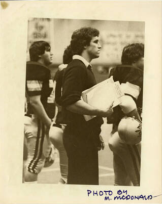 Idaho football team stands with a man who is possibly a coach or staff. The man is holding a notepad that says ""Idaho Army National Guard.""