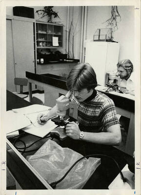 Two biology students looking through microscopes at different tables in the classroom.
