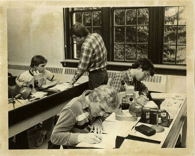Biology students taking notes in a classroom with binocular microscopes on the desks.