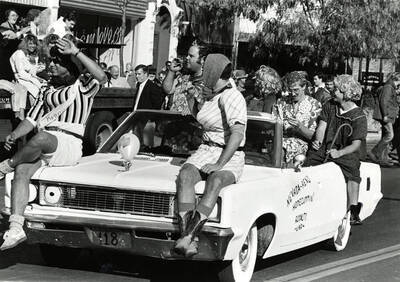 Parade on Main Street. Car reads ""Nevada-Reno Homecummin' [sic] Royalty -UNR-"".