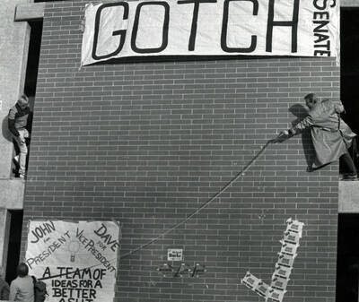 Hans Weger and Seton Foster, members of TKE, hanging campaign signs on the old University Classroom Center (now the Teaching and Learning Center).