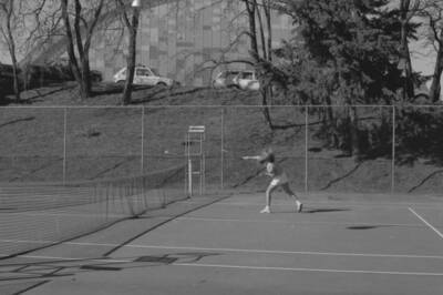 A student playing tennis on the courts just outside of the Physical Education Building.