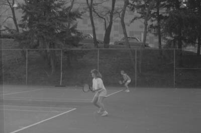 Two students playing tennis on the courts just outside of the Physical Education Building.