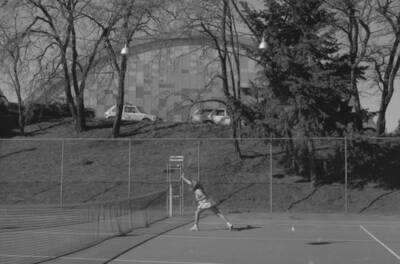 A student playing tennis on the courts just outside of the Physical Education Building.