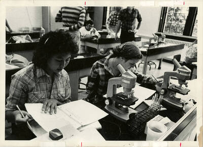 Biology students participating in class activities with microscopes in a classroom.